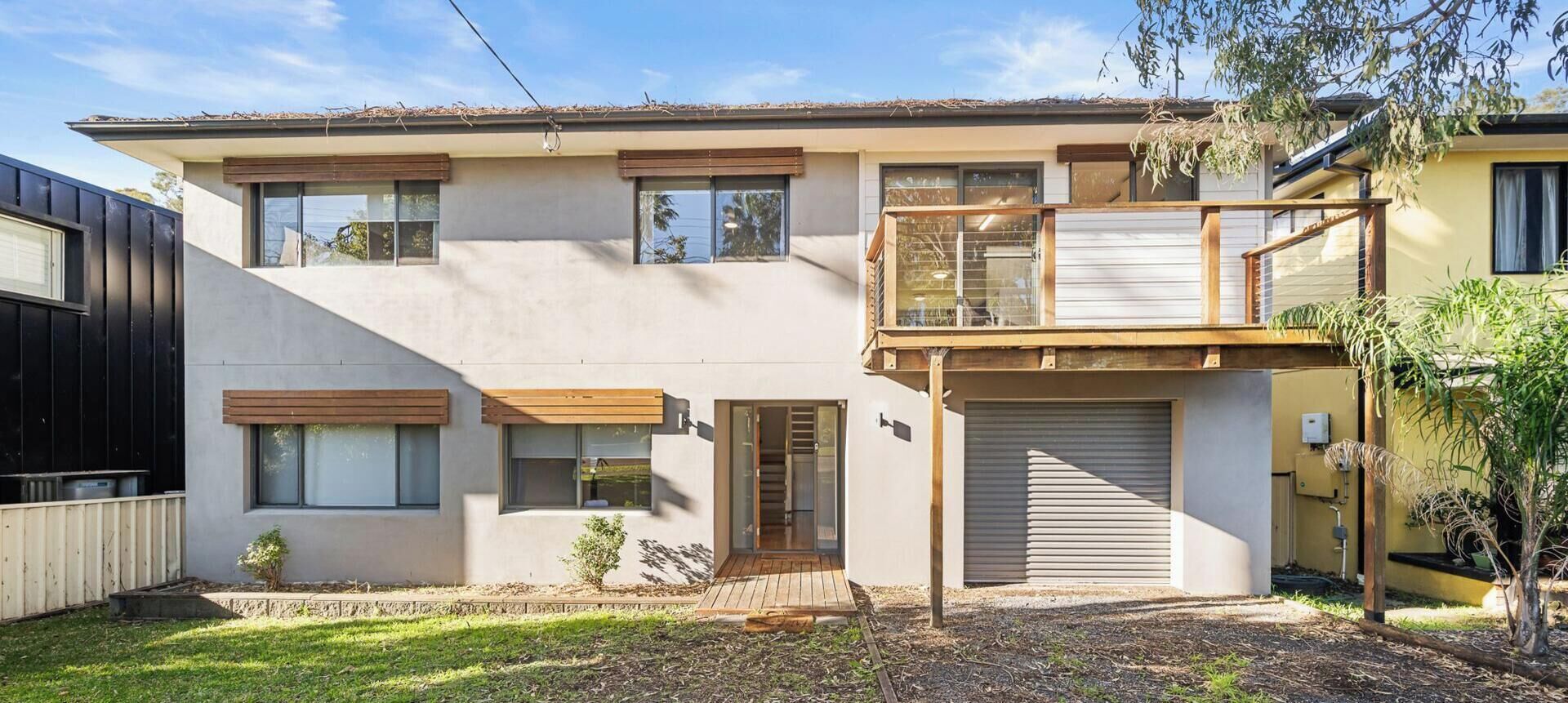 Una casa a due piani con un balcone, un garage e un piccolo giardino antistante.