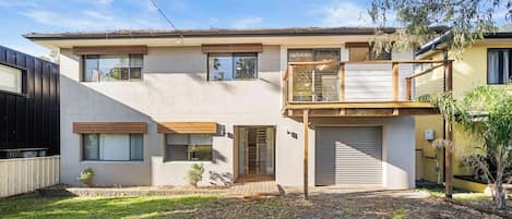 Una casa a due piani con un balcone, un garage e un piccolo giardino antistante.