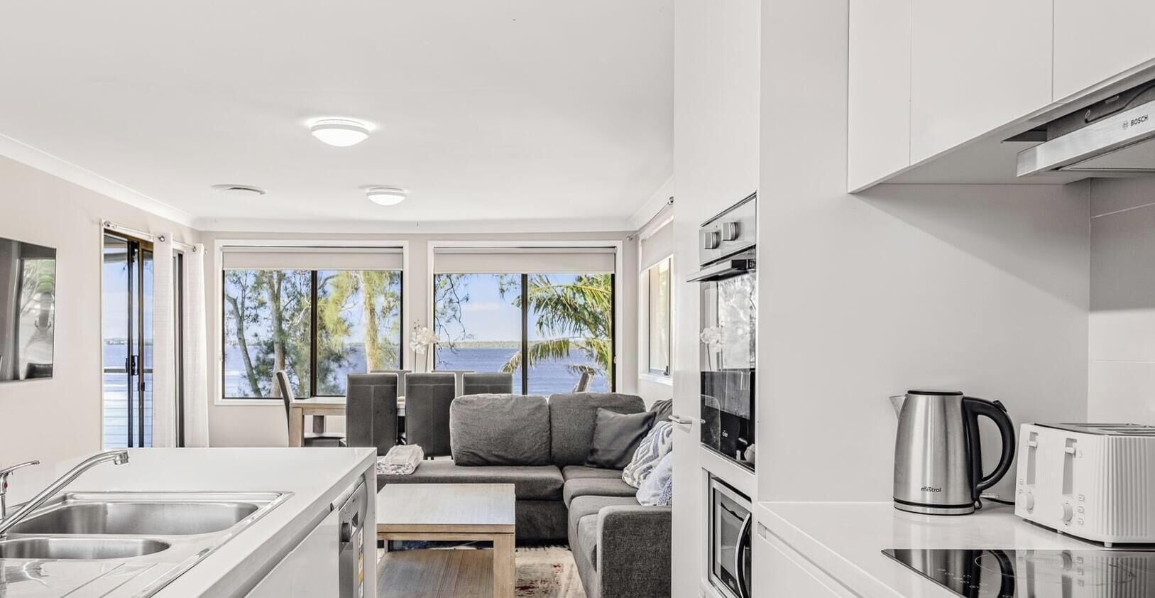 A modern kitchen with a view of the sea, a sofa, and a coffee maker.