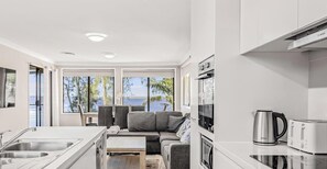 A modern kitchen with a view of the sea, a sofa, and a coffee maker. - Sunrise Waters - Absolute Waterfront Escape (Gorokan)
