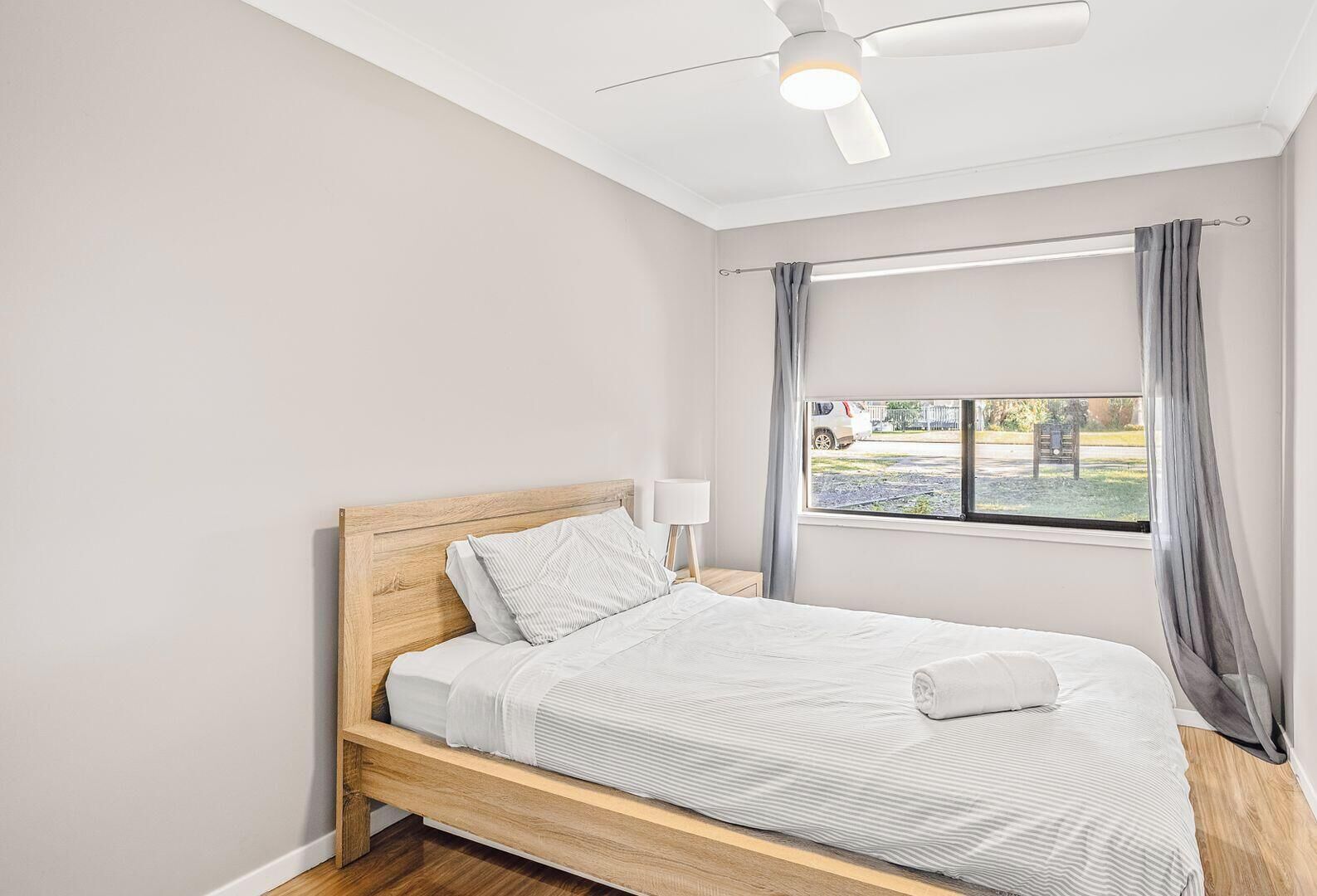 A bedroom with a wooden bed, a window with curtains, and a ceiling fan.