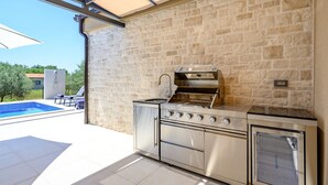 Uma cozinha externa moderna com um painel de parede de pedra, forno embutido e churrasqueira.