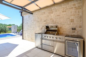 A modern outdoor kitchen with a stone wall backdrop, a built-in oven, and a grill. - Villa Oliver (Istria - Buje) (Buje)