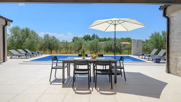 Uma área de piscina ao ar livre com mesa, cadeiras, um grande guarda-sol e espreguiçadeiras.