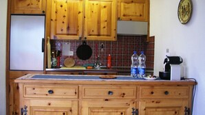 Een keuken met houten kastjes, een betegelde achterwand, een koelkast, een koffiezetapparaat en twee waterflessen.
