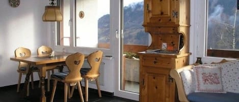 Uma sala de jantar com mesa e cadeiras de madeira, um armário com vários compartimentos e vista para o exterior através de uma porta de vidro.