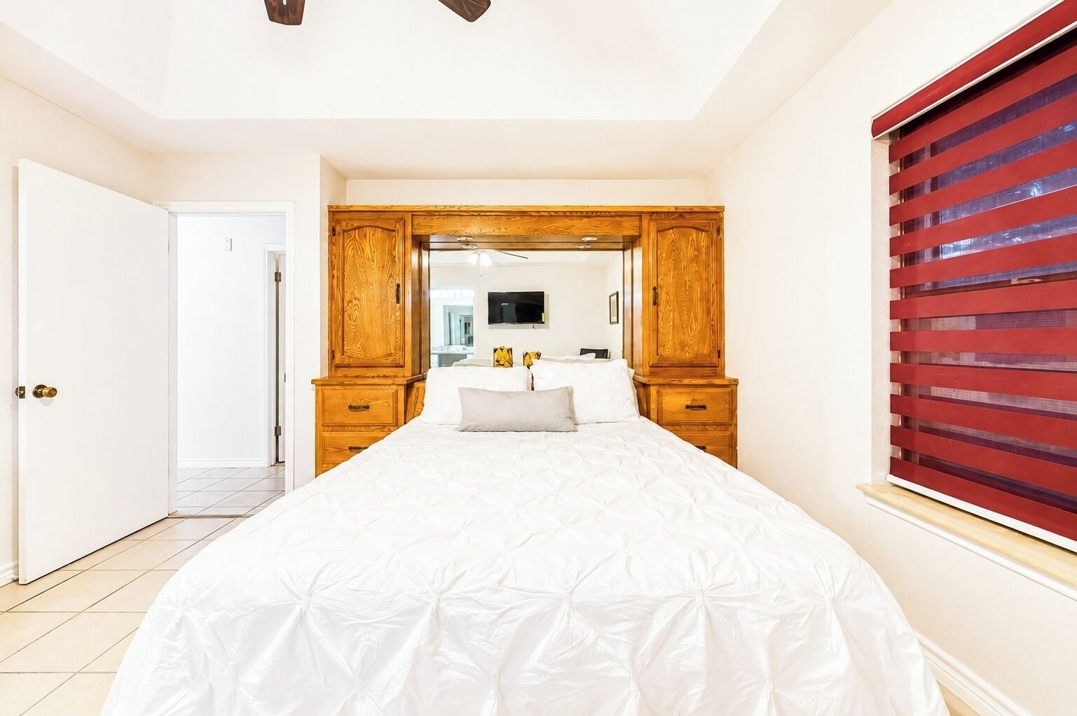 A bedroom with a large bed, wooden wardrobe, and a red-striped window blind.