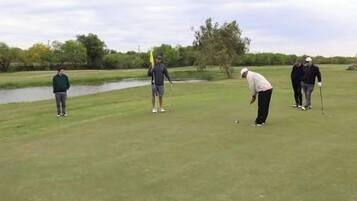 A golf course with a water body and trees in the background.
