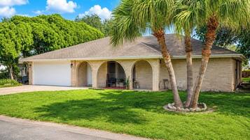 A single-story house with a garage, a covered porch with arches, and a lawn with palm trees.
