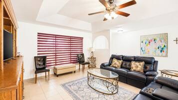 A living room with a sofa, chairs, a coffee table, a TV, and a ceiling fan.