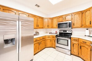 A kitchen with wooden cabinets, a stainless steel refrigerator, a microwave, an oven, and a water dispenser.