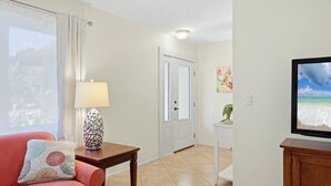 Ein Wohnzimmer mit einer Couch, einem Tisch mit einer Lampe, einem Fernseher und einer Tür.