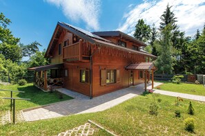 Ein Holzhaus mit überdachter Veranda, einer kleinen Terrasse und einem gepflasterten Auffahrt.