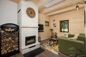Un salon chaleureux avec une cheminée, une horloge, un canapé vert et un décor intérieur en bois.
