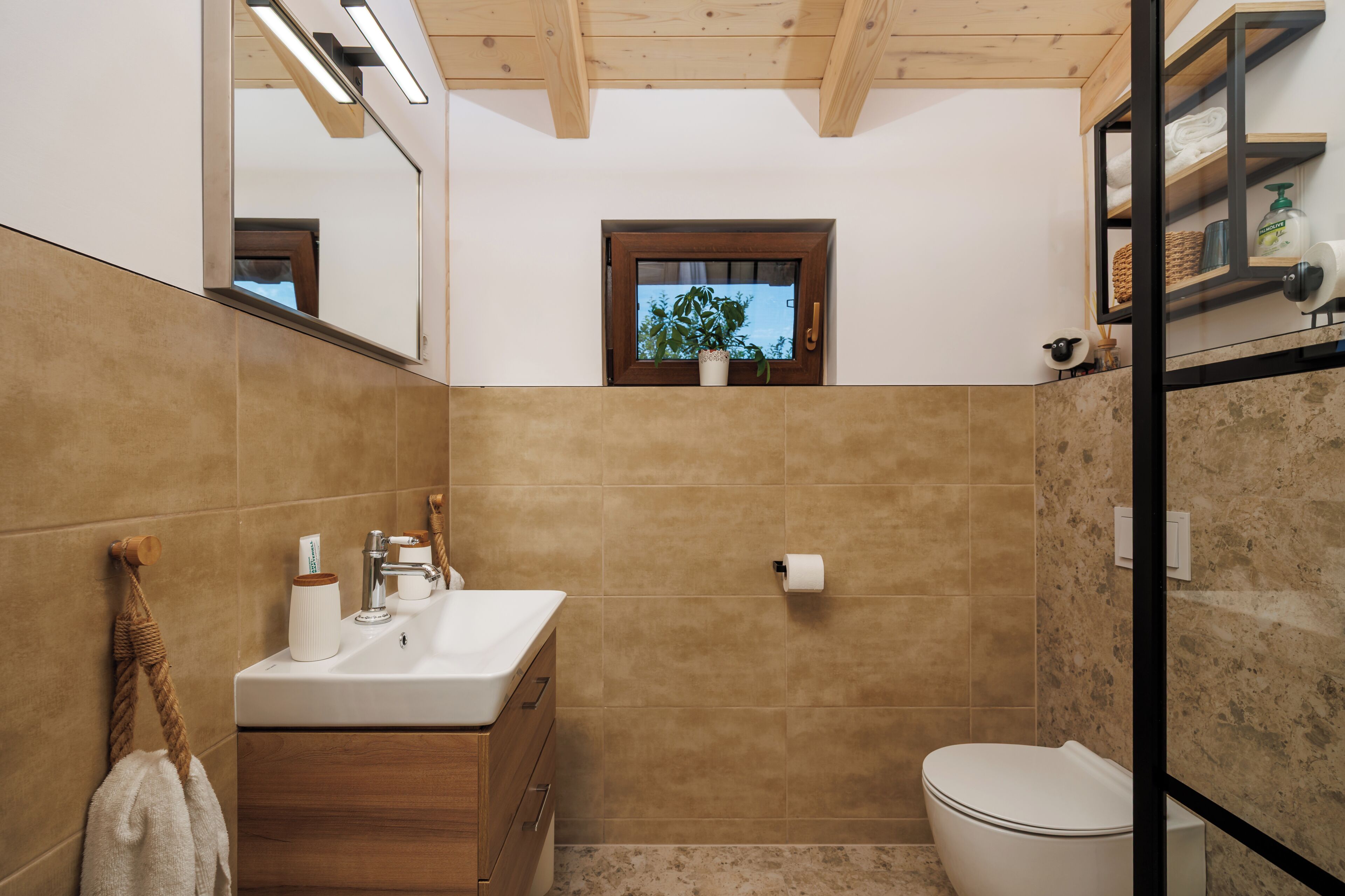 A bathroom with a wooden vanity, a mirror, a toilet, and a small window.