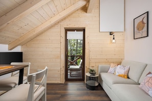 A cozy room with a sloped ceiling, a dining table, a sofa, and a small side table with a plant. - Wooden wellness home with sauna in the heart of Gorski Kotar (Fužine)