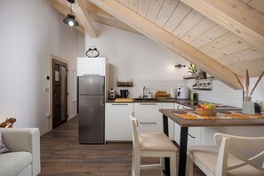 Eine kleine Küche mit Holzbalkendecke, einem Kühlschrank, einem Spülbecken und einem Essbereich mit Stühlen.