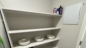 Ein weißer Stauraum mit Regalen, ein schwarzer Slow Cooker und eine Whiteboard.