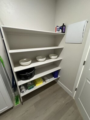 Ein weißer Stauraum mit Regalen, ein schwarzer Slow Cooker und eine Whiteboard.
