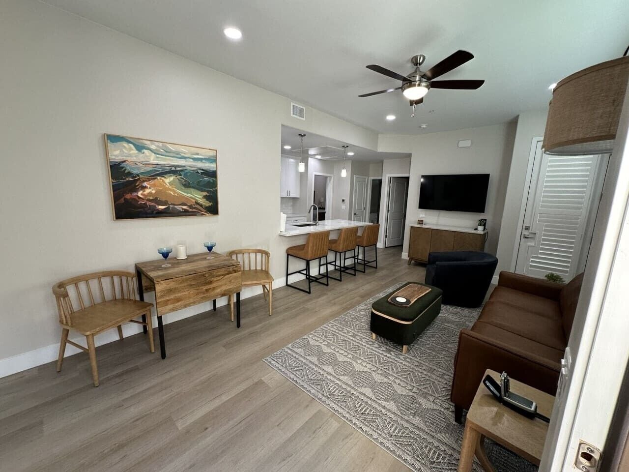 A modern living room with a dining area, a ceiling fan, a flat-screen TV, and a kitchen in the background.