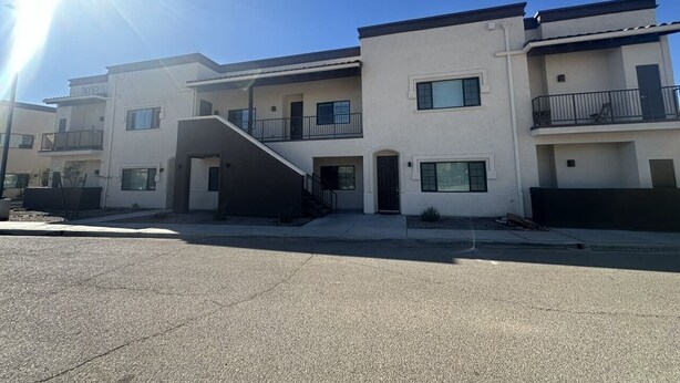 Um edifício residencial de vários andares com telhado plano, varandas e uma escadaria que leva à entrada.