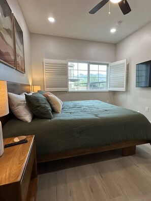 Ein Schlafzimmer mit Bett, Nachttisch, Lampe, Deckenventilator und einem Fenster mit Jalousien.
