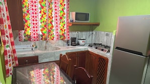 A kitchen with a dining table, chairs, a refrigerator, a microwave, a stove, and a sink. - Grenn House (Sámara)