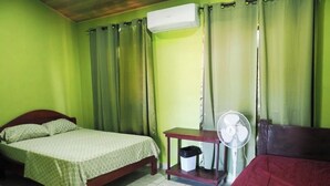 A room with a bed, a bedside table with a fan, and an air conditioning unit. - Grenn House (Sámara)