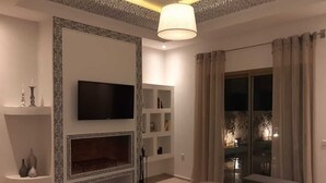 A modern living room with a flat-screen TV, a fireplace, a dining area with a table and chairs, and a large window with curtains. - Exceptional villa with a pool (Essaouira)
