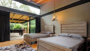 Ein Schlafzimmer mit zwei Betten, Holzbalkendecke, einer Pendelleuchte und Blick ins Freie.