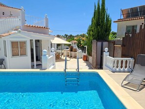 Ein Schwimmbecken mit einer Leiter, eine überdachte Terrasse und ein weißes Gebäude mit einem geFliester Dach.