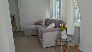 Een moderne woonkamer met een grijze bank, een glazen salontafel en een vaas met bloemen.