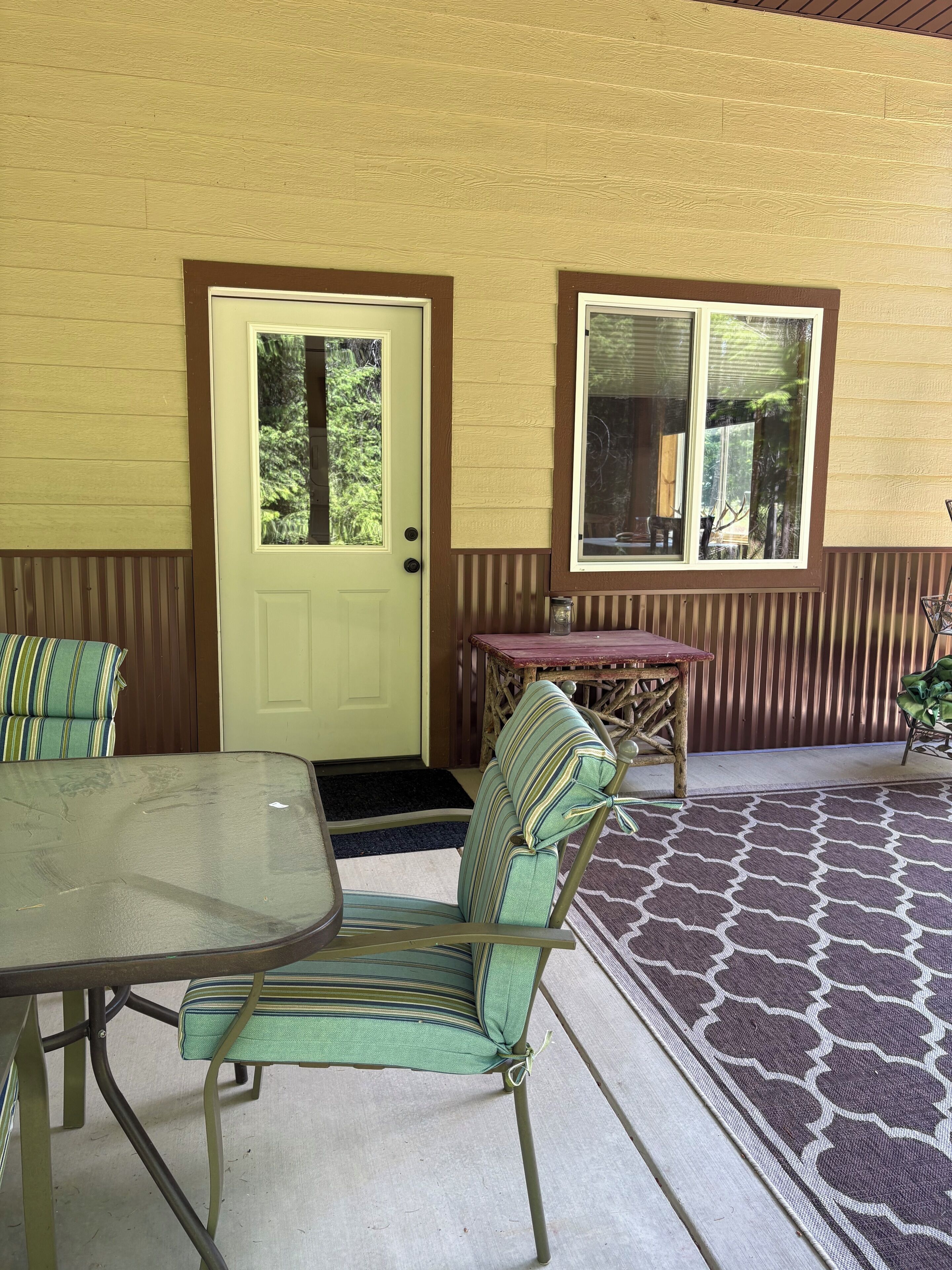 A covered patio area with a table and chairs, a door, and a window.