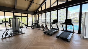 Ein Fitnessstudio mit Trainingsgeräten, großen Fenstern und einem Zickzack-Fußbodenmuster.