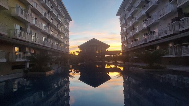 Ein symmetrisch angelegter Gebäudekomplex mit Balkonen, einem zentralen Spiegelbecken und einem Sonnenuntergang im Hintergrund.