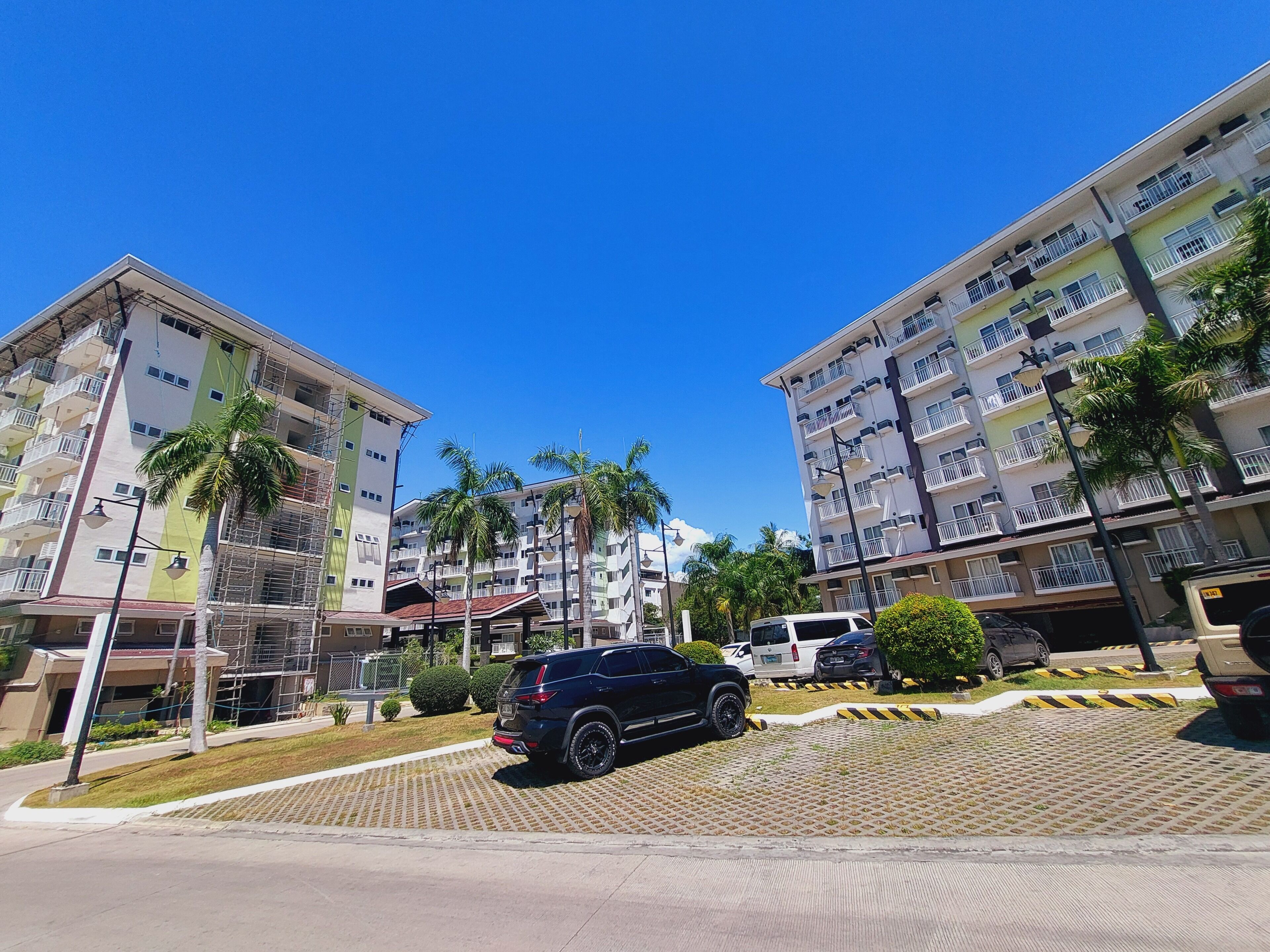 A multi-story residential building with balconies, palm trees, and a parked SUV.