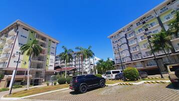 A multi-story residential building with balconies, palm trees, and a parked SUV.