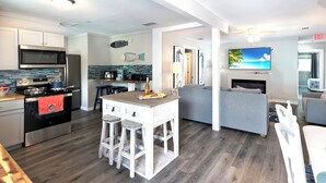 Ett modernt kök med en köksö i mitten, en matplats med en grå soffa och ett vardagsrum med en tv.