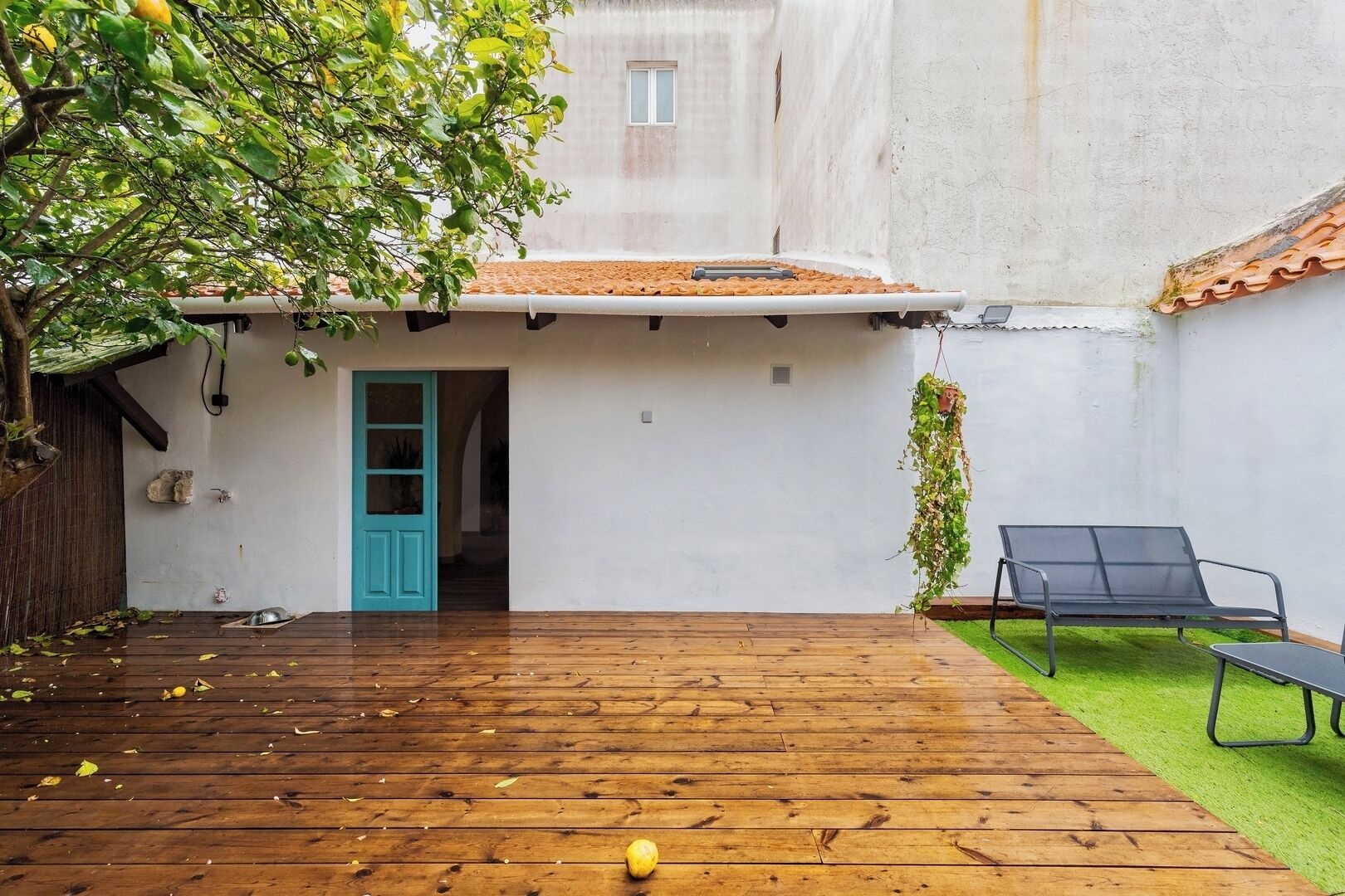 A wooden deck with a blue door leading to a white building, a hanging plant, and a black lounge chair.