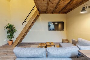 A modern living room with a sloped ceiling, a large flat-screen TV mounted on the wall, a wooden staircase, and a seating area with a sofa and a small table. - Palmela Oasis Apartment II, By Home Match (Palmela)