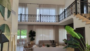 Een ruime woonruimte met een hoge plafond, een trap en een balkon met een zwarte leuning.