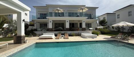 A modern two-story house with a swimming pool, outdoor seating, and a well-maintained garden.