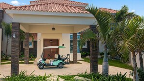 Een modern huis met een overdekte oprit, een golfkar en palmbomen.