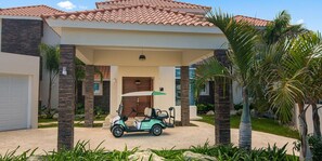 Un edificio residencial con entrada porticada, un carrito de golf y palmeras.