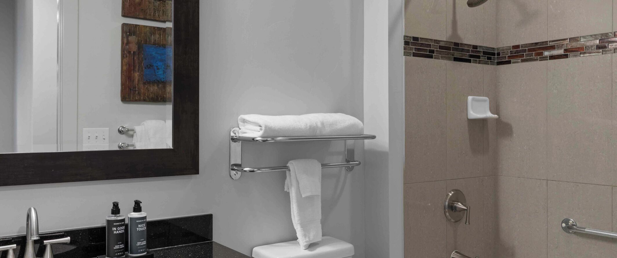 A bathroom with a toilet, a towel rack, a shower, and a sink with toiletries.