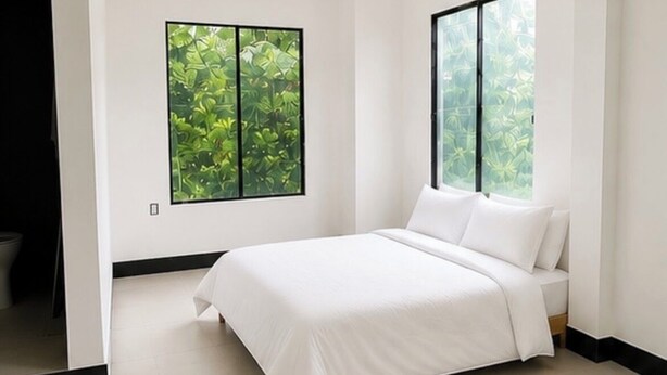 A modern bedroom with a large bed, two windows, and a view of greenery.