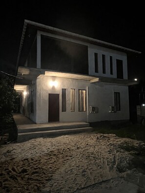 A modern two-story house with a well-lit entrance and a visible outdoor area.