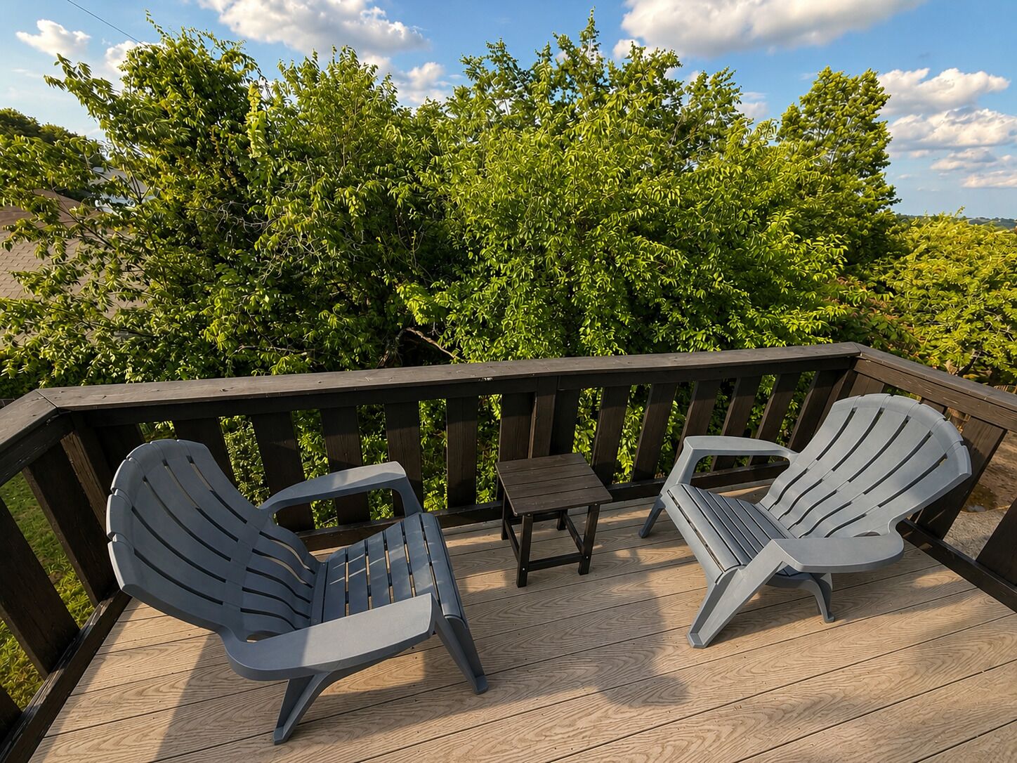 A wooden deck with two Adirondack chairs and a small table.
