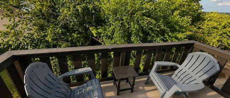 A wooden deck with two Adirondack chairs and a small table.