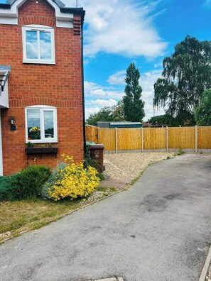 A residential brick house with a driveway, a wooden fence, and a yellow flowering plant. - House Sleeps 4 with Parking and Garden (Newark)